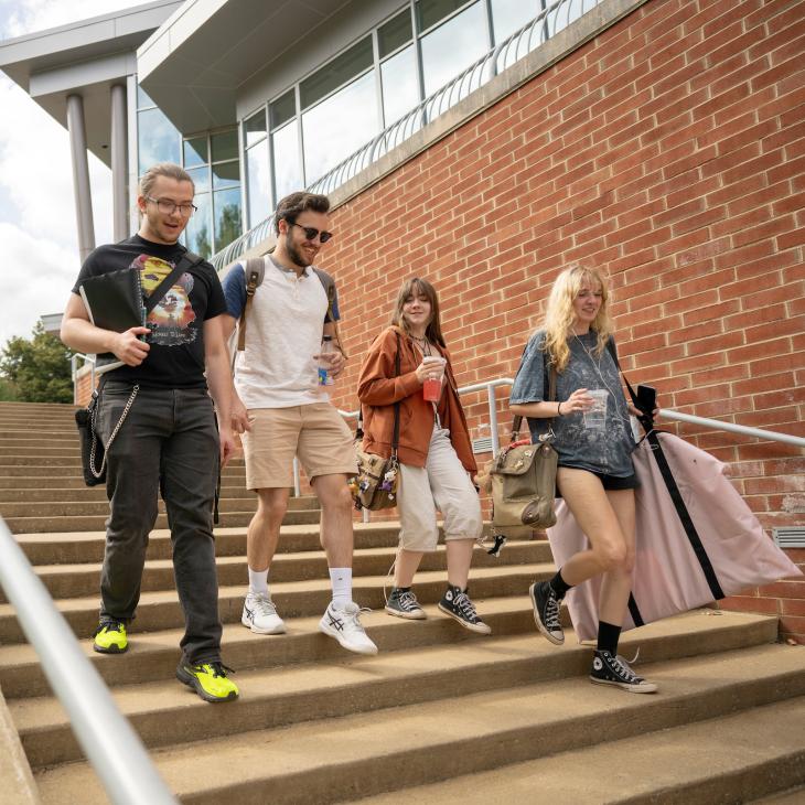 Four students walk down the steps outdoors beside the Performing Arts Center
