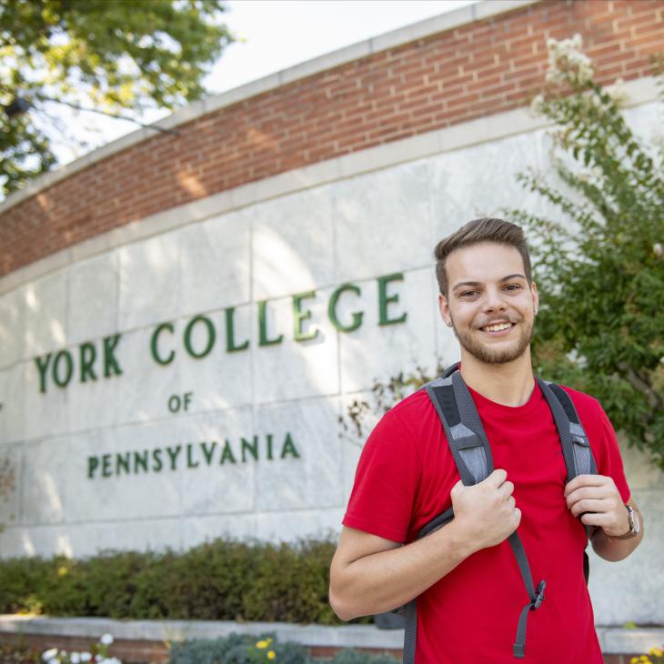 A student smiling in front of the York College of Pennsylvania wall.