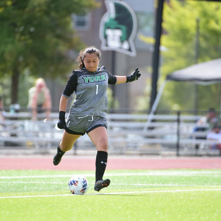 Teresa González-Herrera kicks a soccer ball on field in her YCP goalie uniform.