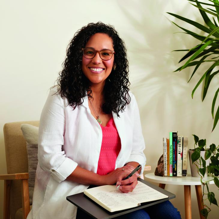 Thaís Carrero smiles from her seat in an office sitting area, papers on her lap..