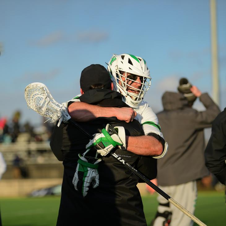 Two lacrosse players embrace as they celebrate on the field.