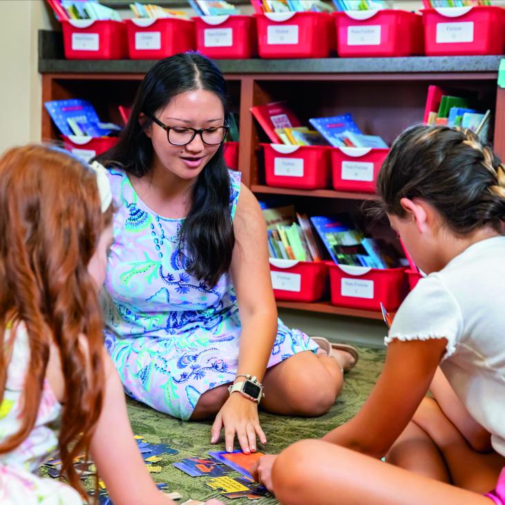 Jasmine Sariano sits on the floor with three young students, working on an activity in an elementary classroom.