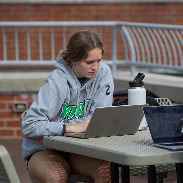 Student sitting outside working on their laptop.