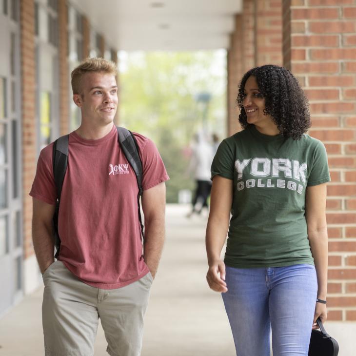 A male and female student walk together in Wolf Hall Courtyard on the York College Campus