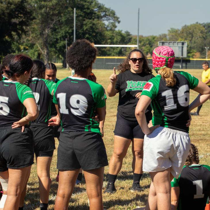 A group of women's rugby players listening to their coach.