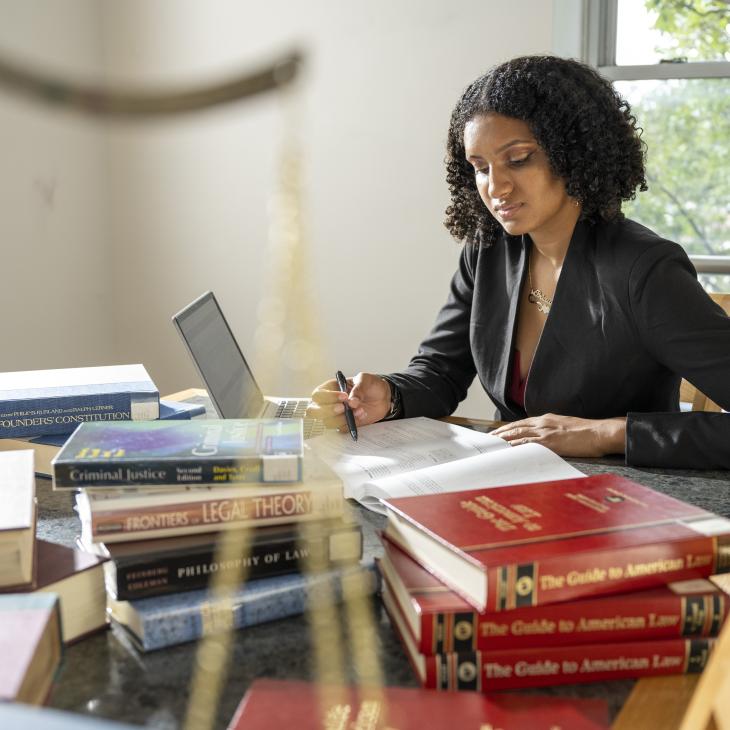 Person in professional attire reading in a sunlit room with legal texts scattered on the table.