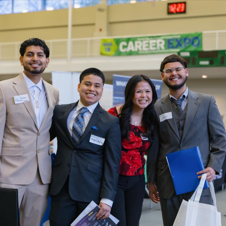Four students stand together in suits and dress clothes under a banner that reads Career Expo.